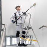 Man standing on a ladder wearing Portwest workwear in black and white using a long paint roller to paint a wall