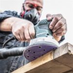 Tradesman wearing protective mouth covering sanding wood with Makita sander in the foreground